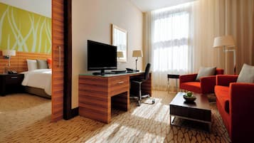 A hotel room with a bed, a desk with a TV, a red sofa, and a coffee table.