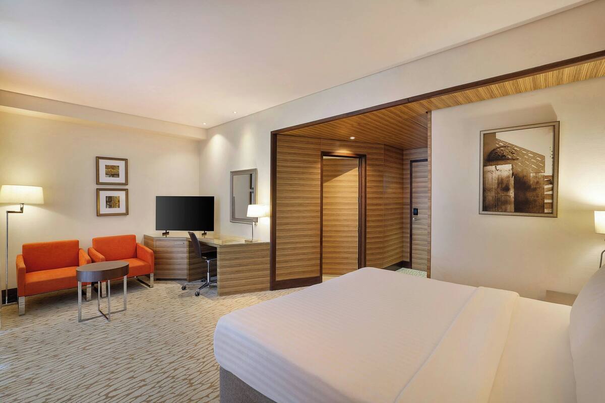 Ein Hotelzimmer mit einem Bett, einer Sitzecke, einem kleinen Tisch, einem Schreibtisch mit Computer, einem Fernseher und einer Holzwand.