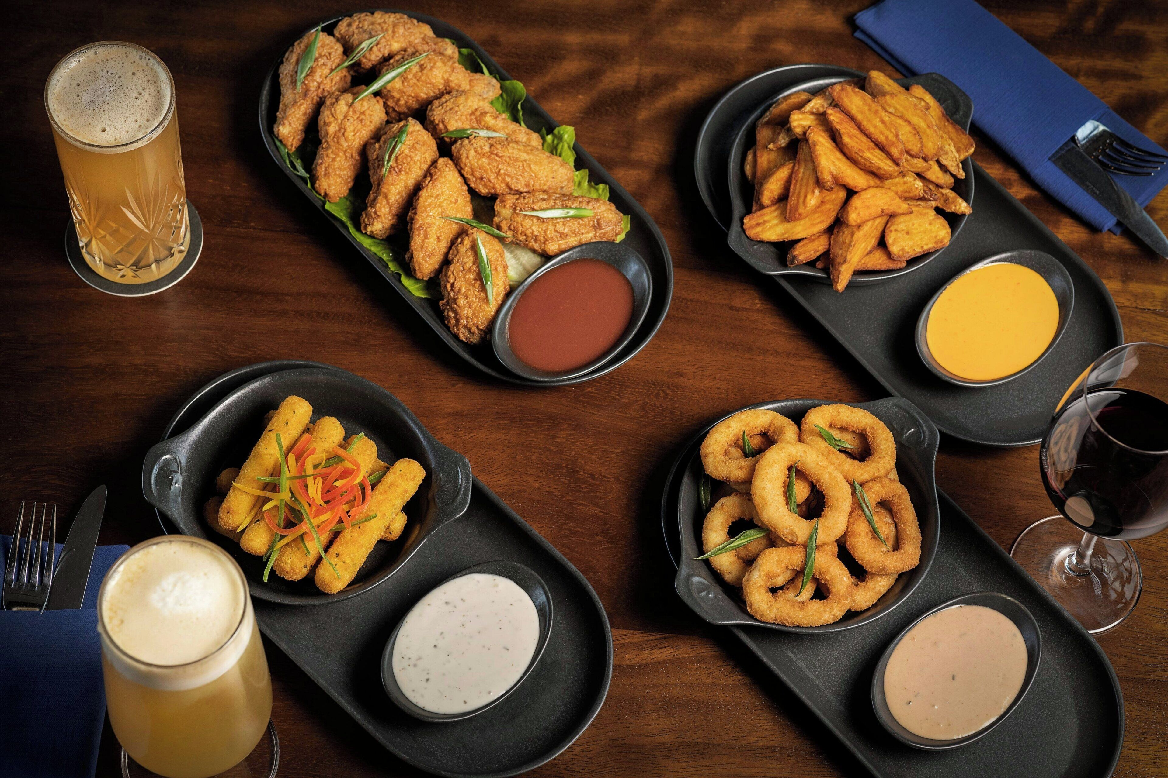 A table with various fried foods, including chicken tenders, onion rings, and fries, accompanied by different dipping sauces.