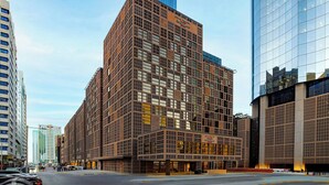Een modern gebouw met een rastergevel en meerdere ramen, omringd door andere hoge gebouwen.