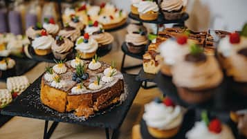 Diversos doces à mostra, incluindo cupcakes, bolos e pastelaria, dispostos em travessas de ardósia preta.