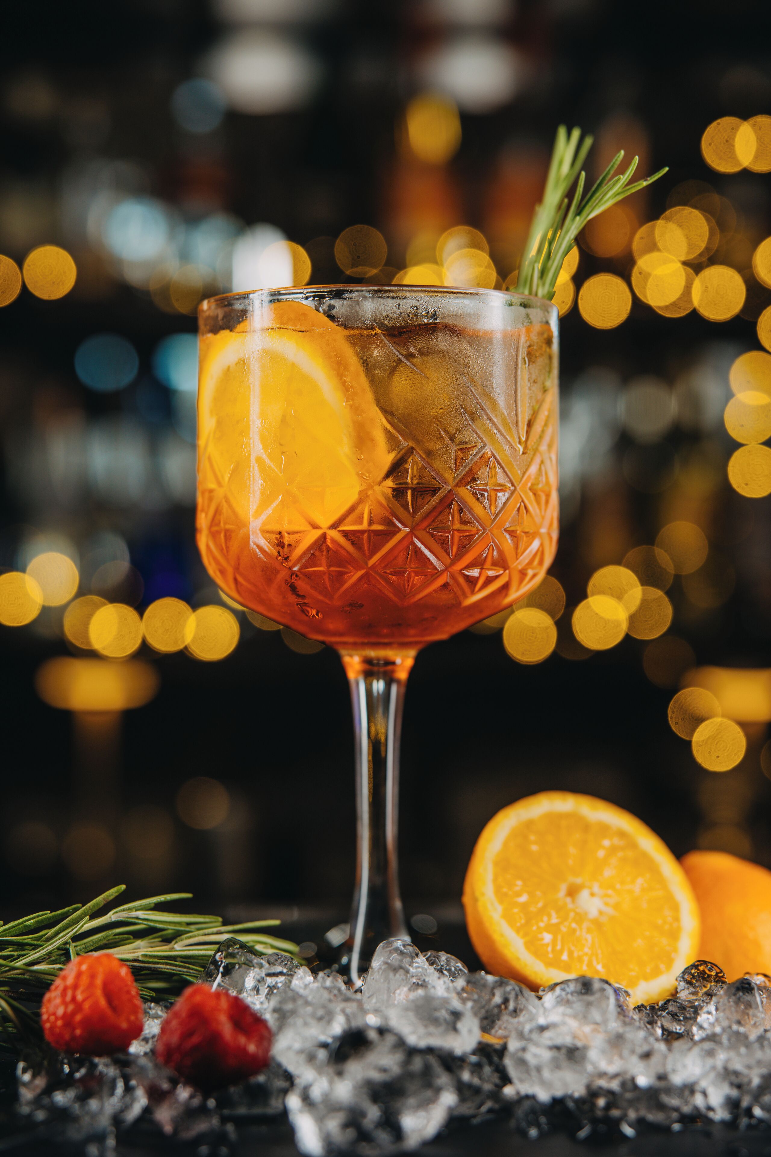 Een cocktailglas met ijs, een oranjeschijfje en een takje rozemarijn.