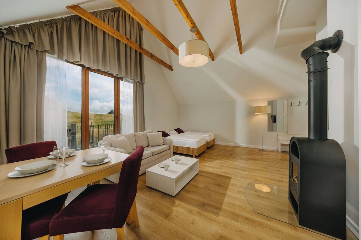 Un dormitorio tipo loft moderno con un gran ventanal, chimenea integrada, sofá y zona de comedor.