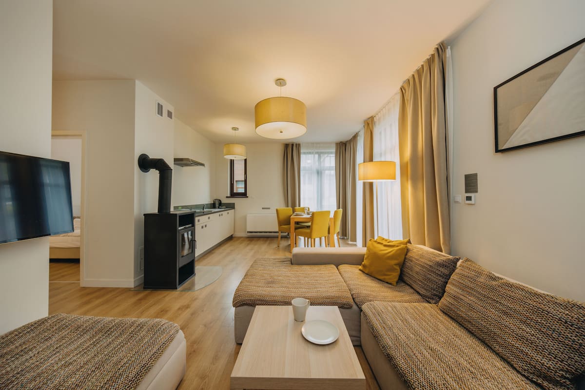Una sala de estar moderna con un sofá, una mesa de centro y un televisor. Se observa una cocina al fondo con una mesa de comedor y sillas.