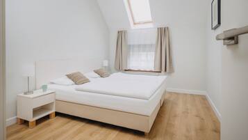 Un dormitorio con cama, mesita de noche, lámpara y ventana con cortinas.
