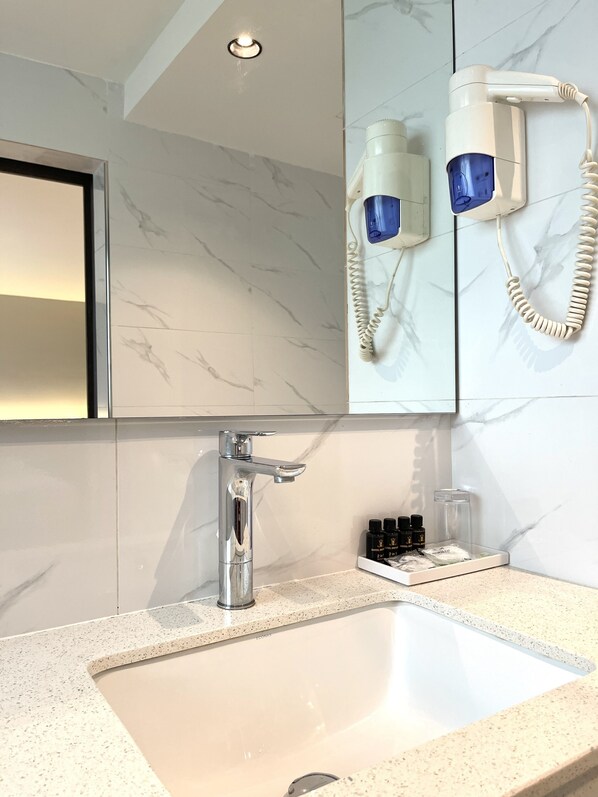 Une salle de bain moderne avec un grand miroir, un robinet chromé et un sèche-cheveux fixé au mur.