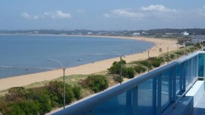 A coastal view with a sandy beach, a clear sky, and a few buildings in the distance. - Apart Hotel Punta Azul (Punta del Este)