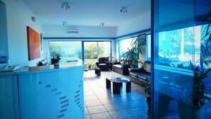 A modern hotel lobby with a reception desk, seating area, and large windows offering views of the outdoors. - Apart Hotel Punta Azul (Punta del Este)