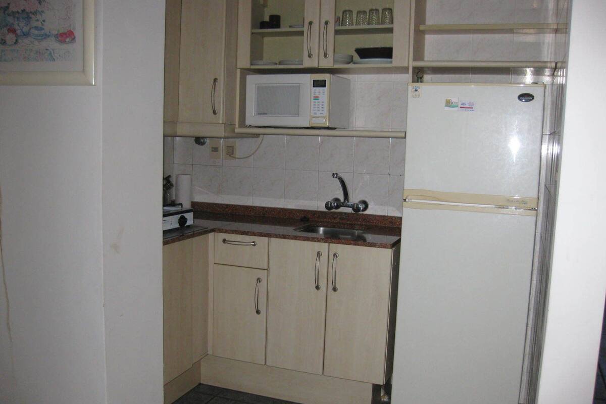 Una pequeña cocina equipada con microondas, refrigerador, lavamanos y armarios.