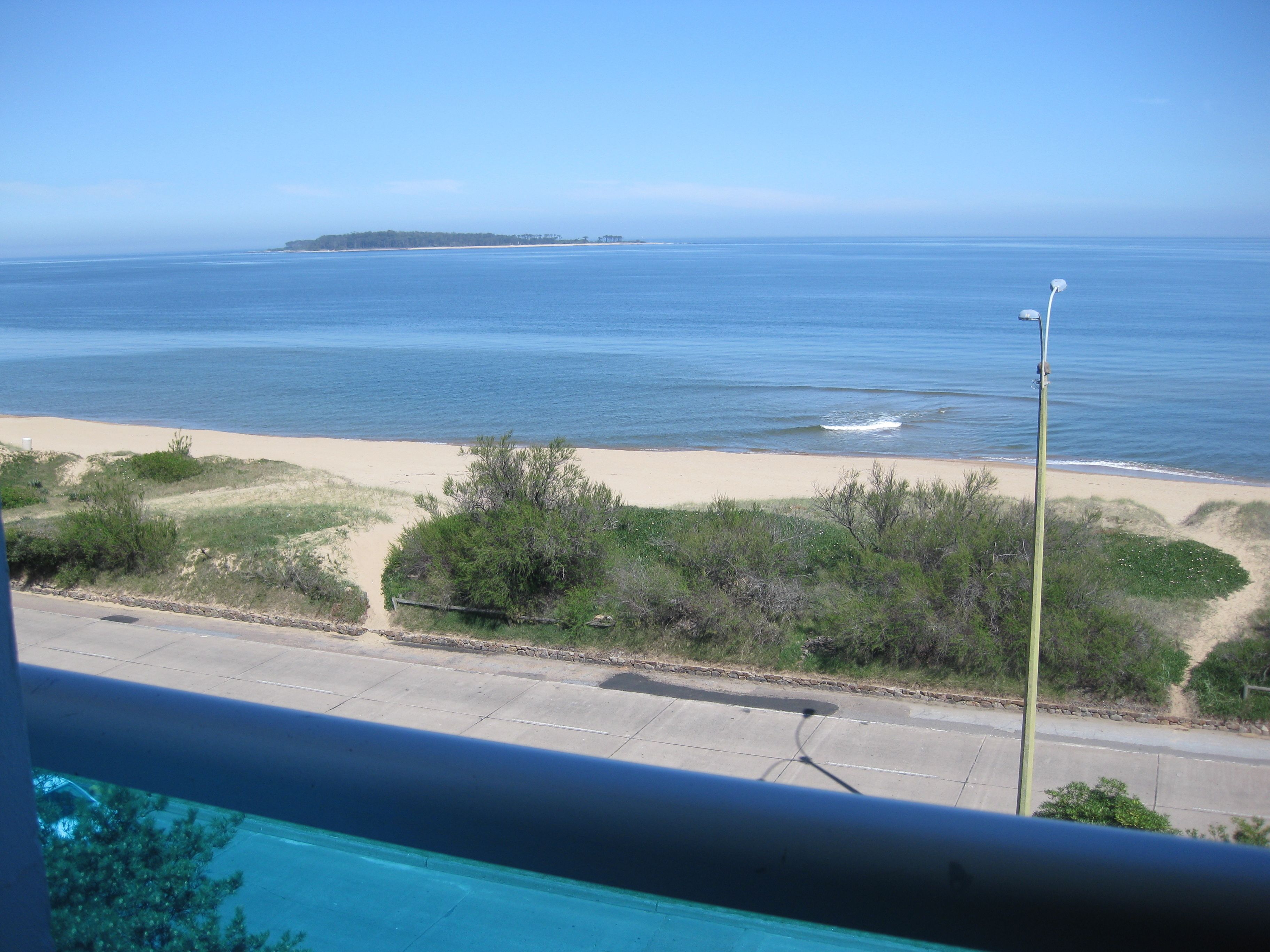 A view of a beach with a clear sky, a sandy shore, and a body of water.
