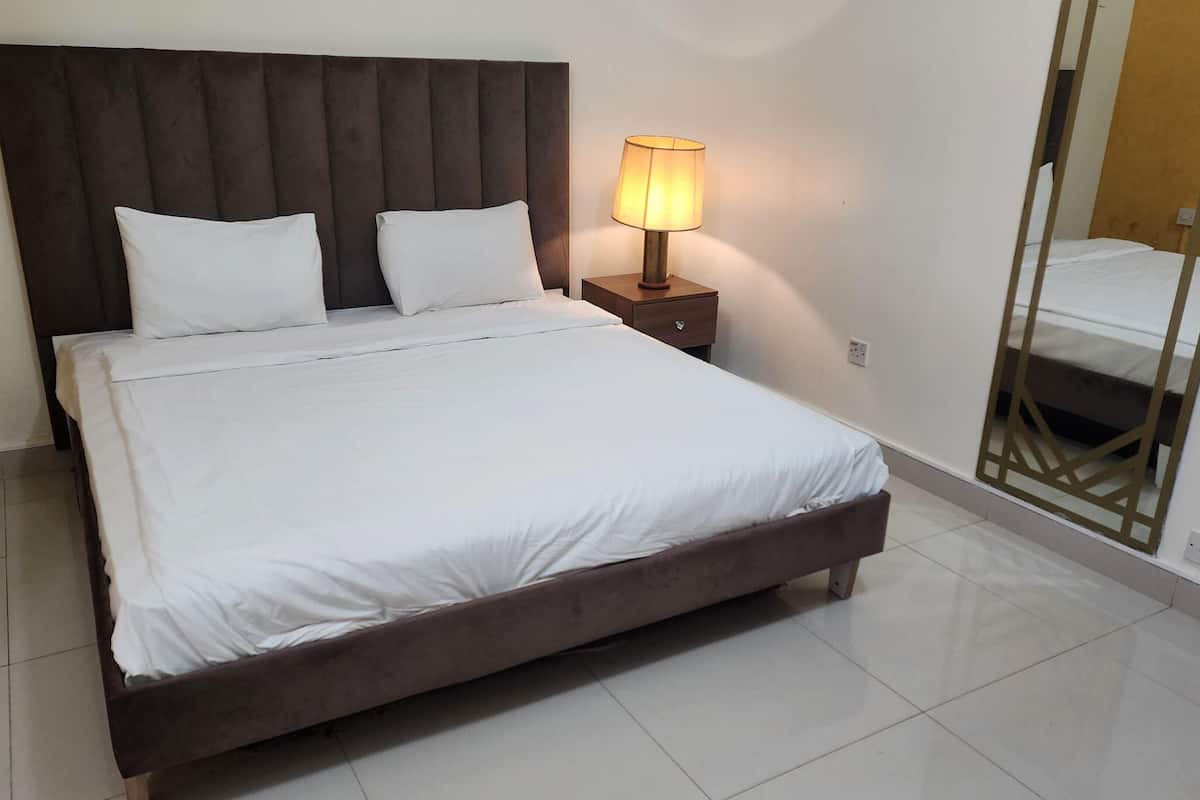 A neatly made bed with white linens, a dark headboard, and a bedside lamp.
