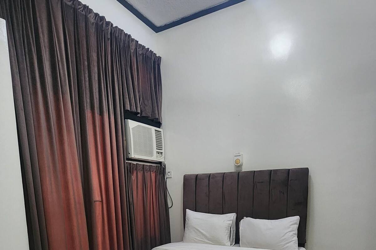 A bedroom with a bed, curtains, an air conditioning unit, and a ceiling light.
