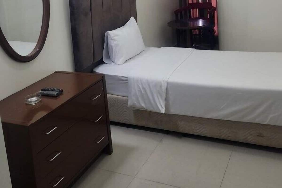 A bedroom with a bed, a dresser, a round mirror, a clock, and a window with curtains.