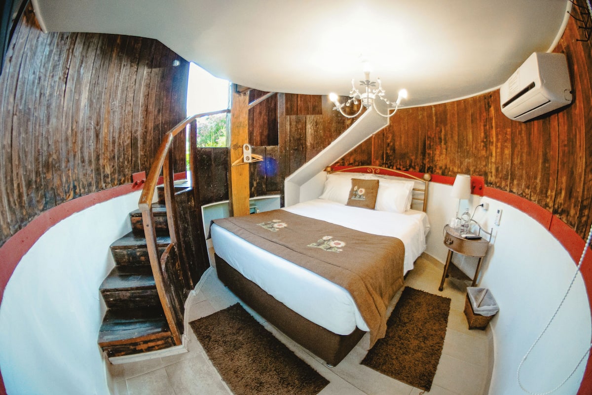 A bedroom with a bed, a nightstand, a chair, a staircase, and a chandelier.