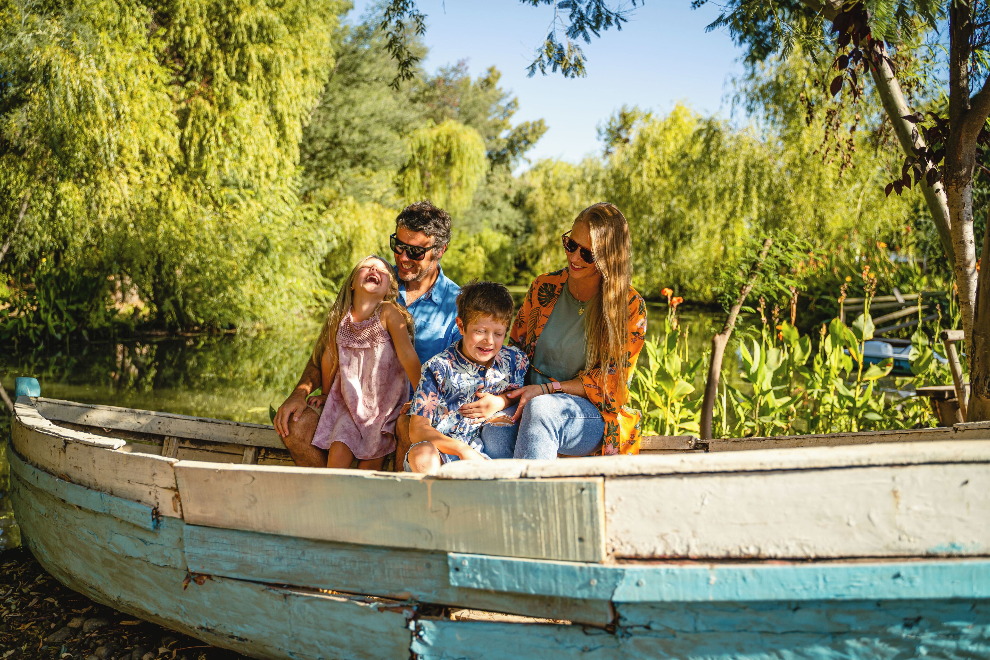 A family in a small boat on a calm body of water surrounded by lush greenery.