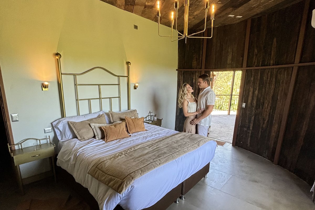 A spacious bedroom with a large bed, wooden ceiling, and a view of the outdoors.