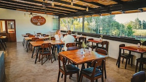 Interior de restaurante con mesas y sillas de madera, un letrero que dice 'DECAVAS RESTAURANT', y ventanas grandes con vistas a zonas verdes.
