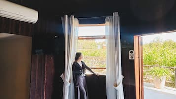 A room with a bed, a window with curtains, a hanging light fixture, and an air conditioning unit.
