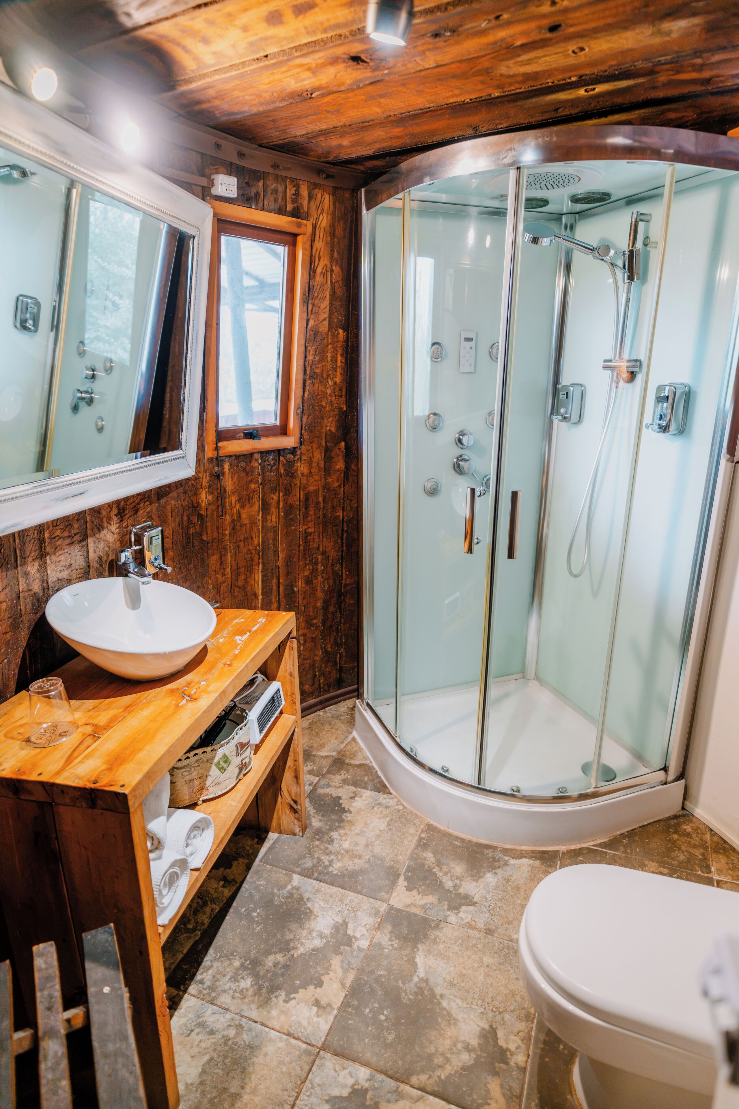 A bathroom with a wooden vanity, a glass-enclosed shower, and a white toilet.