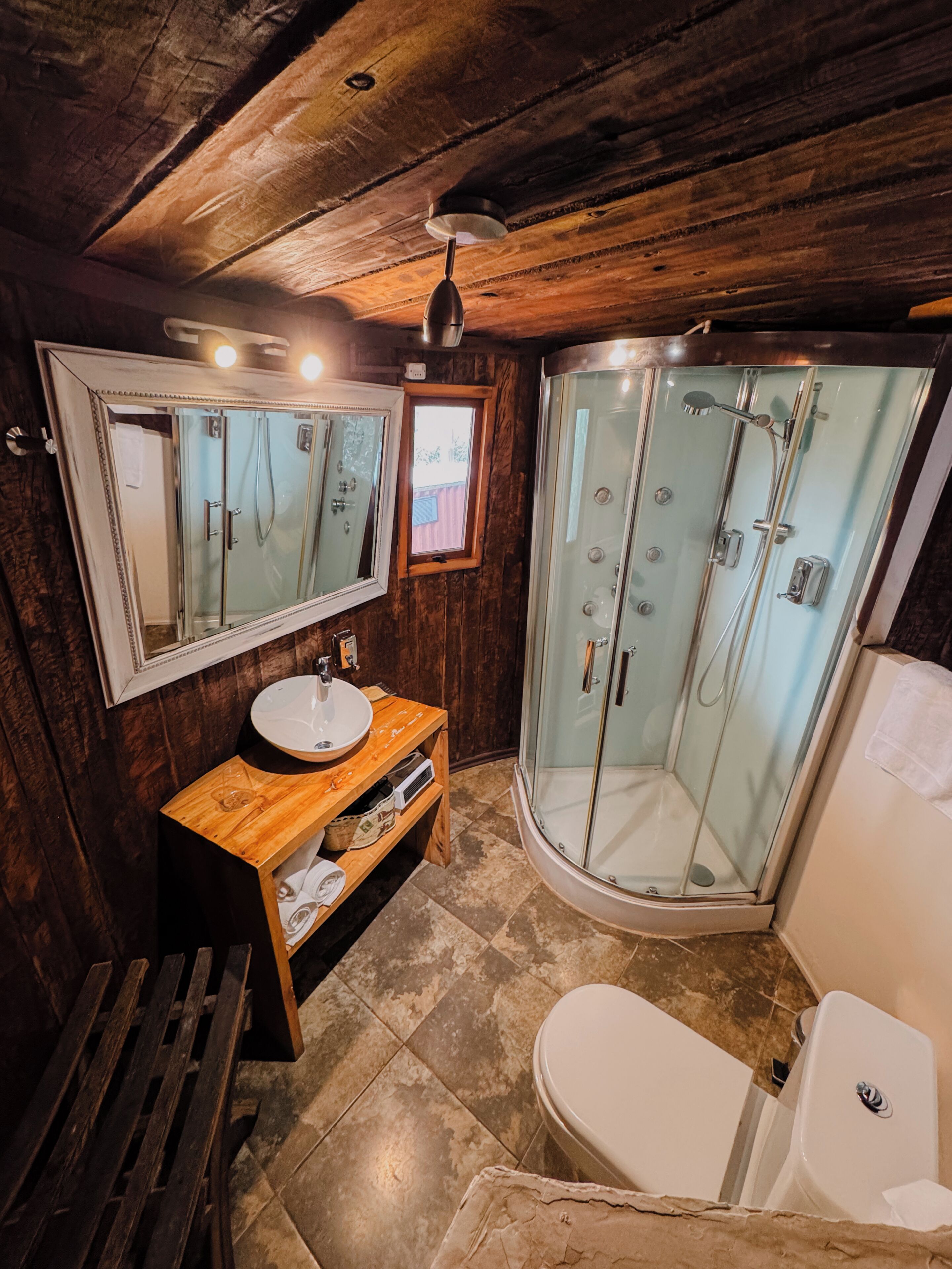 A bathroom with a wooden interior, a glass shower enclosure, a white sink, and a toilet.