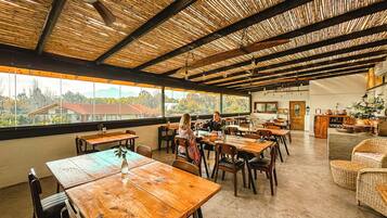 Un comedor interior con mesas y sillas de madera, ventanas amplias y techo de bambú.