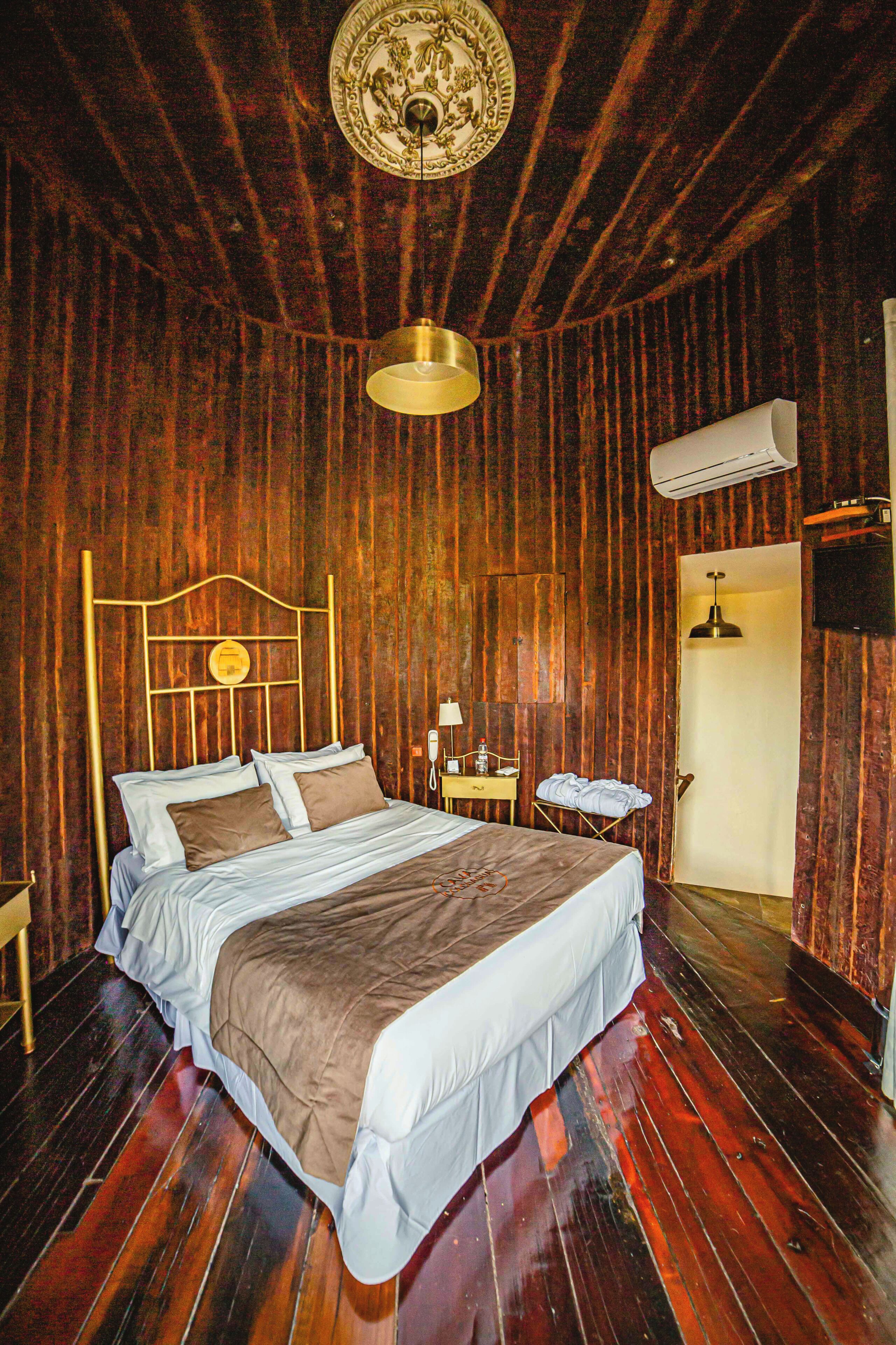 A wooden-paneled room with a bed, a bedside table, a lamp, and an air conditioning unit.