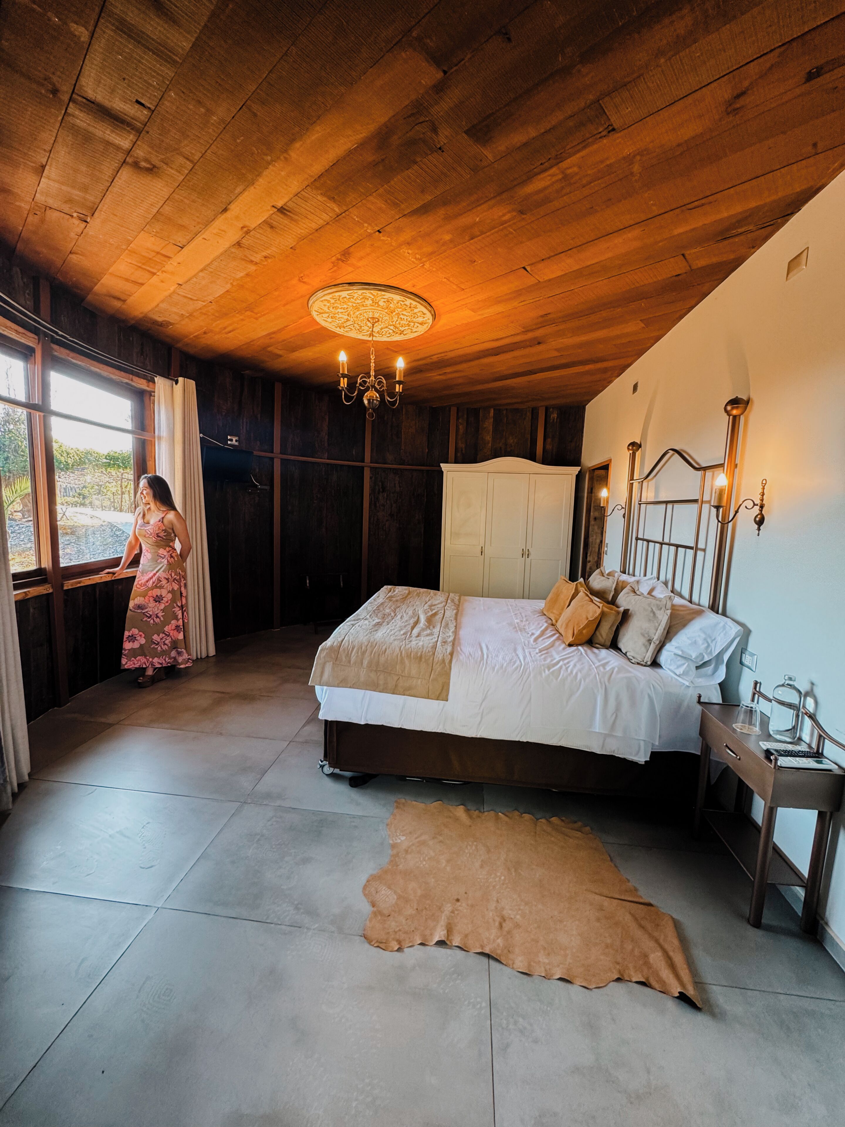 Un dormitorio con cama, candelabro, armario y vistas a través de una ventana.