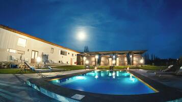 Piscina com espreguiçadeiras, área de estar coberta e um edifício ao fundo.