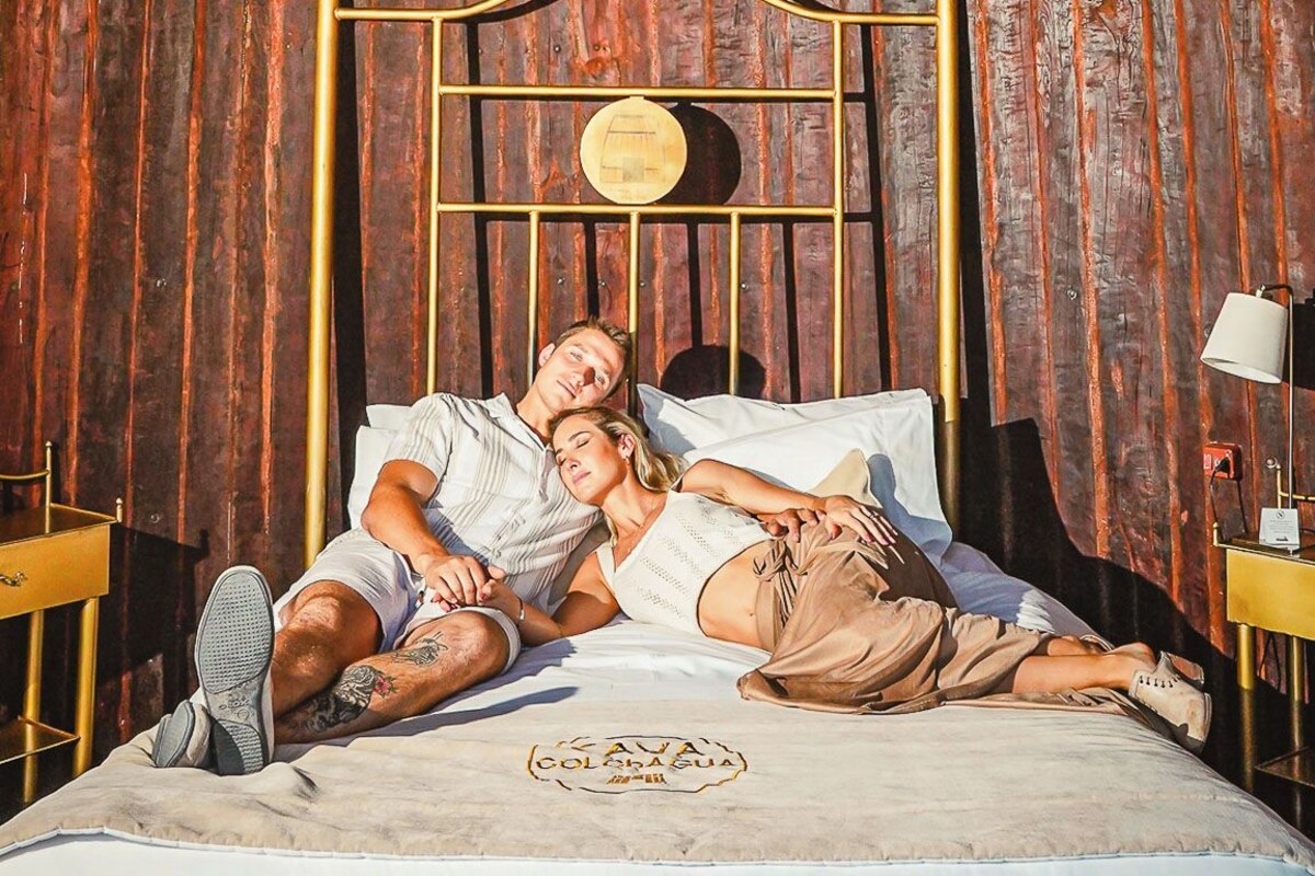 Una cama con cabecera de metal, una l ámpara colgante y una pared de madera con tablones verticales.