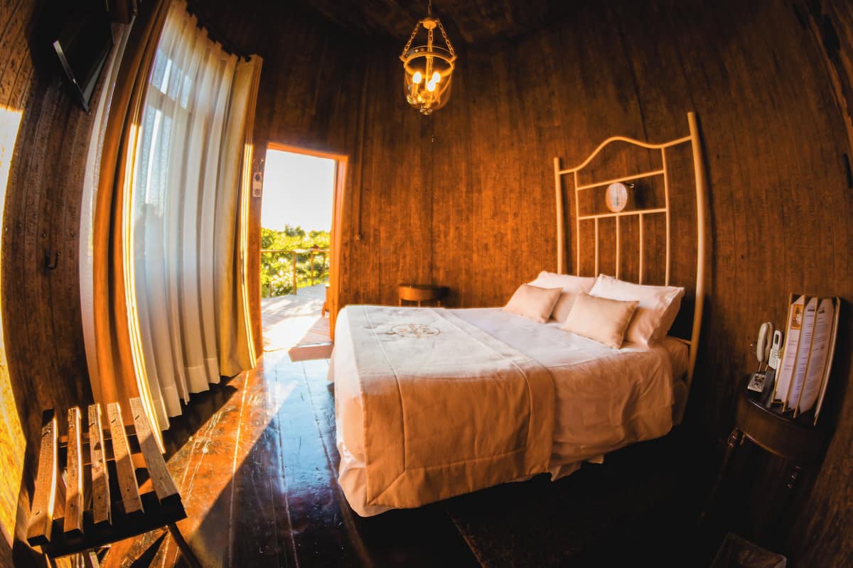 A wooden room with a bed, a wooden bench, and a hanging light fixture.
