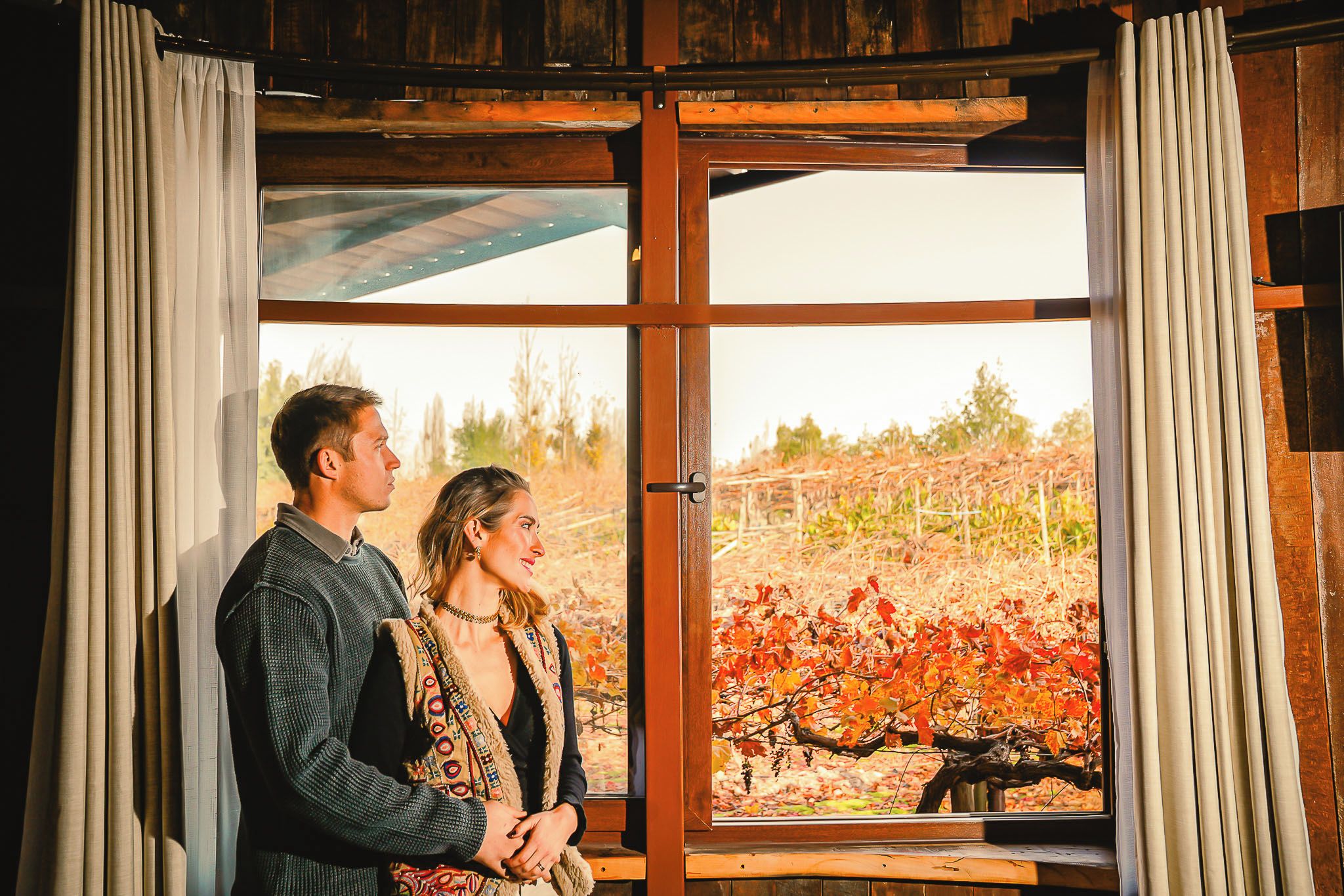 A couple standing by a window with a view of autumn leaves.