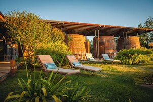 Un patio con sillones de descanso, una terraza de madera y grandes tanques cilíndricos en un jardín.