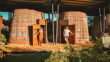 Dos grandes barriles de madera con puertas, un muelle de madera y follaje.