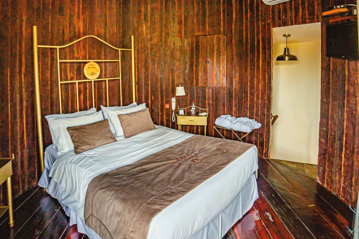 A wooden-paneled room with a bed, a bedside table, a lamp, and an air conditioning unit.