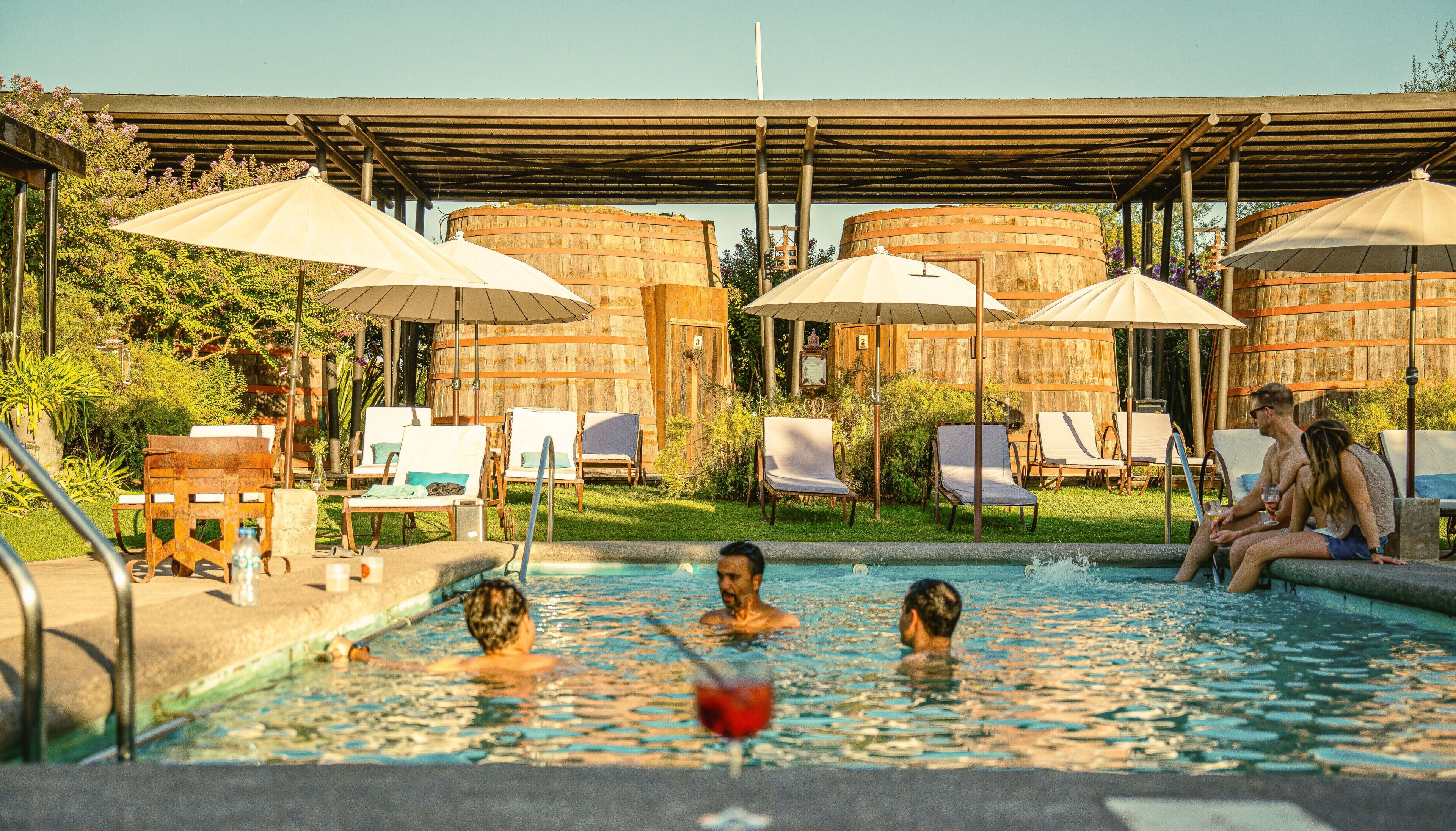 A pool area with lounge chairs and umbrellas, surrounded by wooden structures.