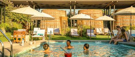 A pool area with lounge chairs and umbrellas, surrounded by wooden structures.