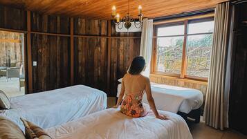Una habitación con paredes y techo de madera, dos camas, una araña y vistas a través de una ventana.