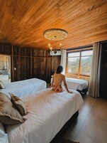Una habitación con paredes y techo de madera, dos camas, una araña y vistas a través de una ventana.