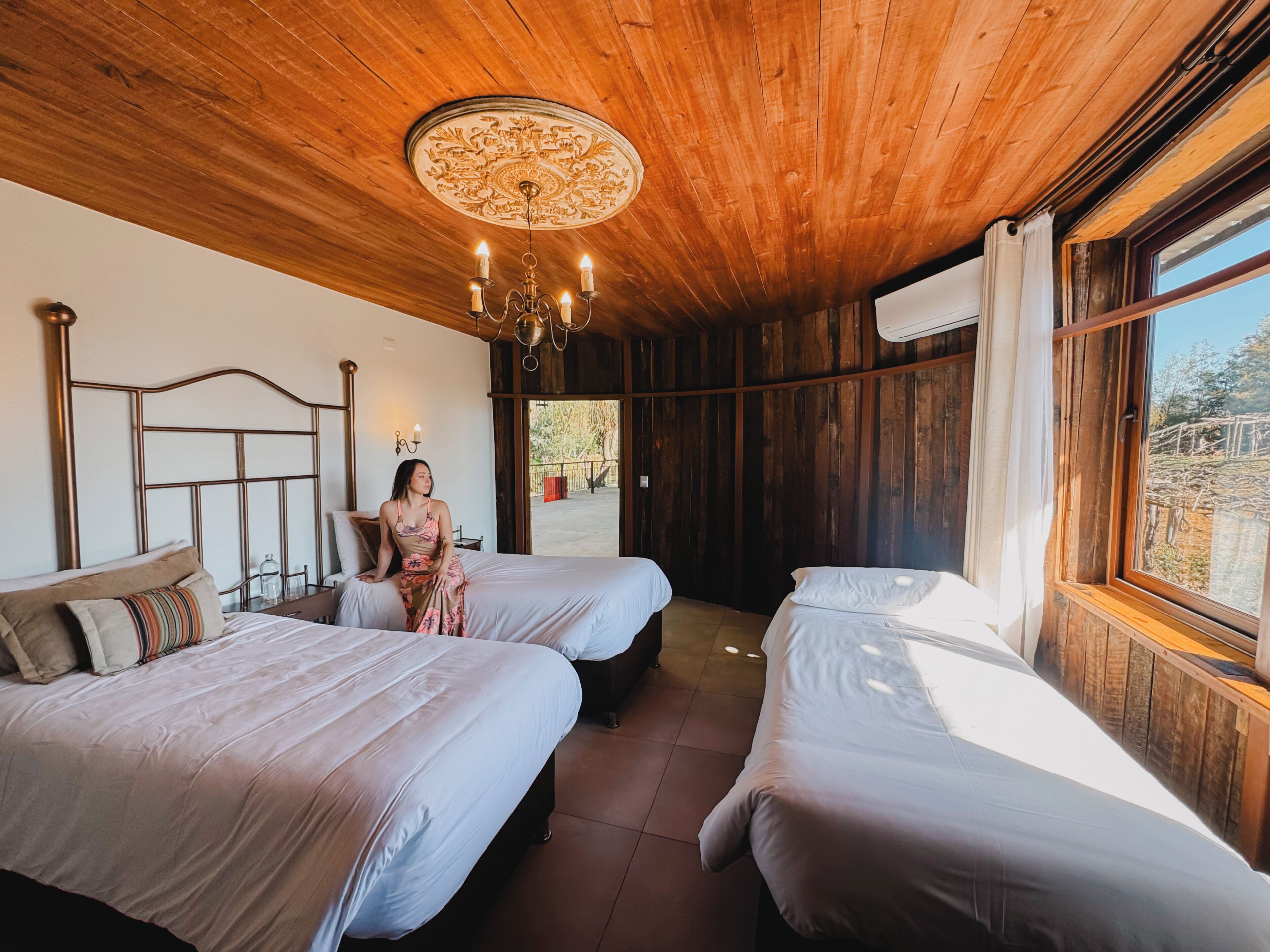 A room with two beds, a chandelier, and a window with a view.
