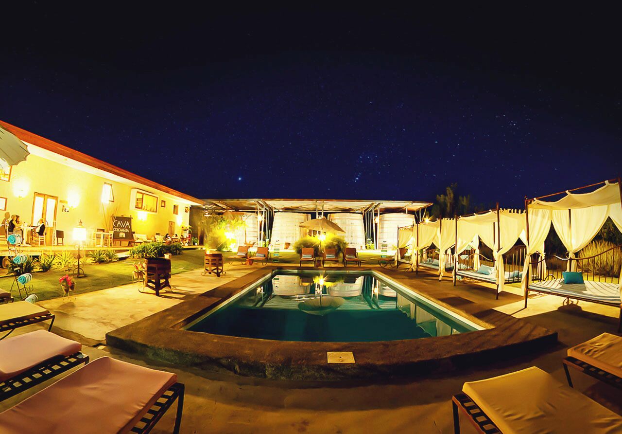 A pool area with lounge chairs, a hot tub, and a building with a yellow facade.