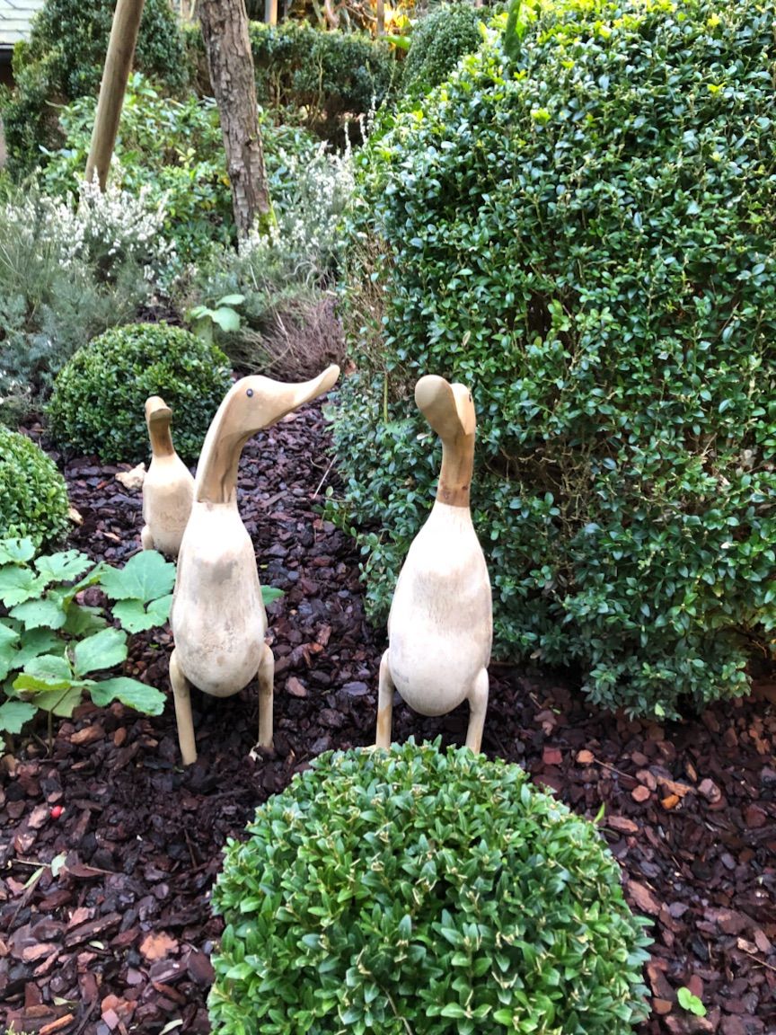 A garden with three wooden sculptures of animals and various shrubs.