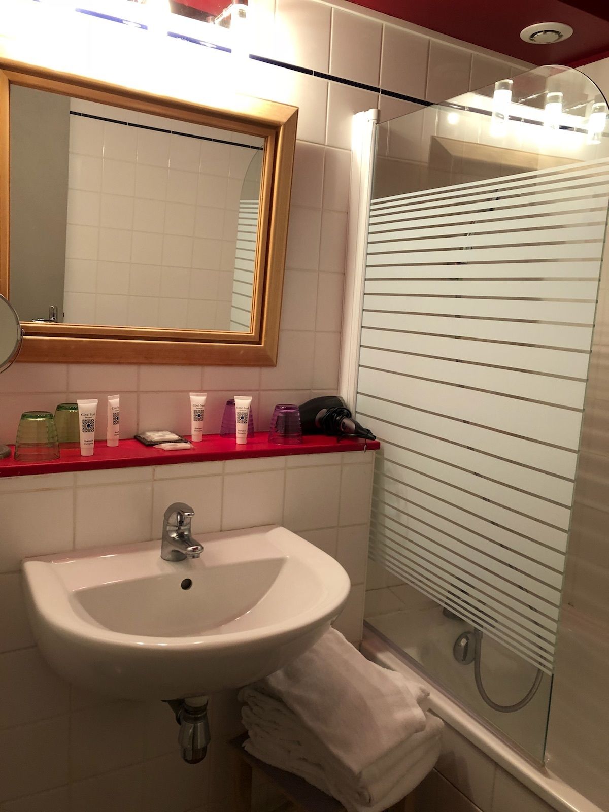 Une salle de bain avec un lavabo blanc, un miroir avec un cadre en bois et une cabine de douche en verre.