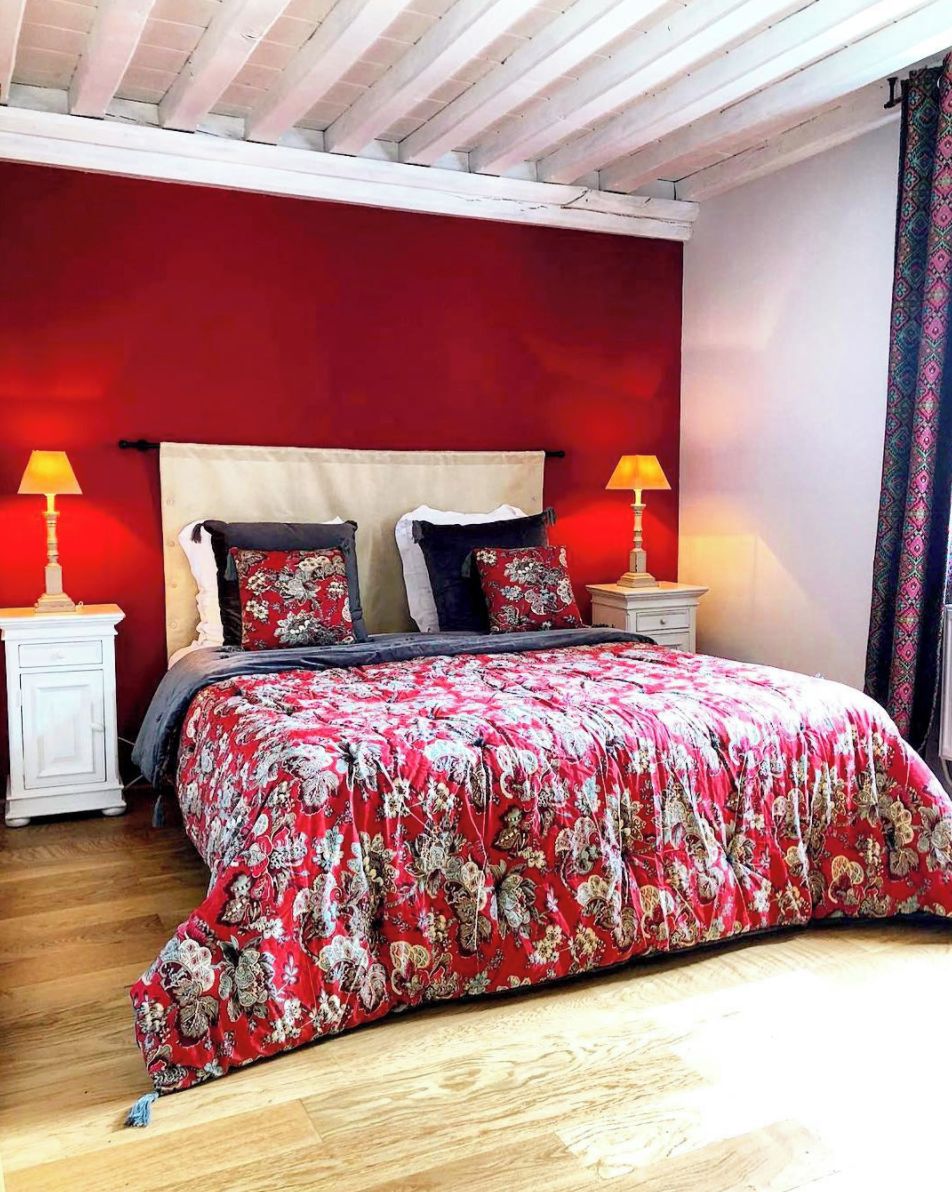 Un dormitorio con pared roja, cama con ropa de cama floral, dos lámparas de noche y suelo de madera.