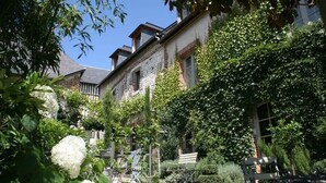 A courtyard with a brick building, surrounded by lush greenery and white hydrangea flowers. - La Cour Sainte Catherine (Honfleur)