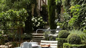 A garden with a table and chairs, surrounded by lush greenery and a building with exposed timber framing. - La Cour Sainte Catherine (Honfleur)