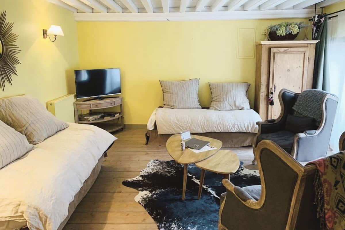 Ein gemütliches Zimmer mit zwei Betten, einem Fernseher, einem kleinen Tisch und einem Sessel.