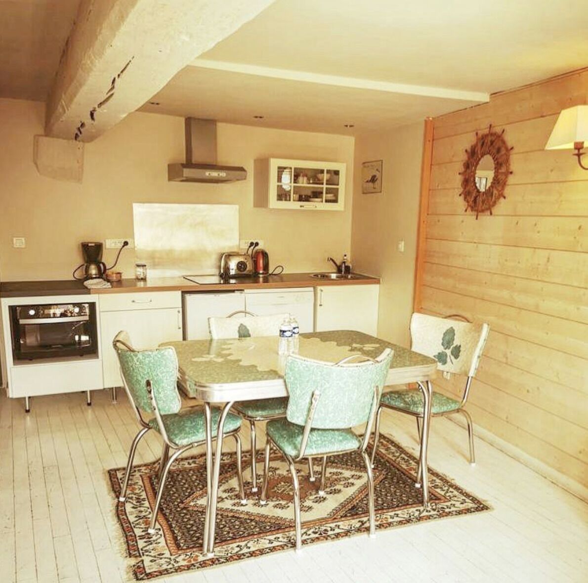 Una cocina compacta con una mesa de comedor y sillas, horno empotrado, cafetera y microondas.