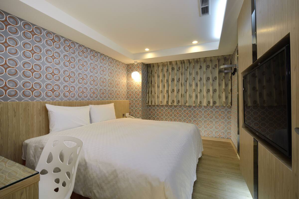 A hotel room with a bed, a TV, a desk, and a chair.