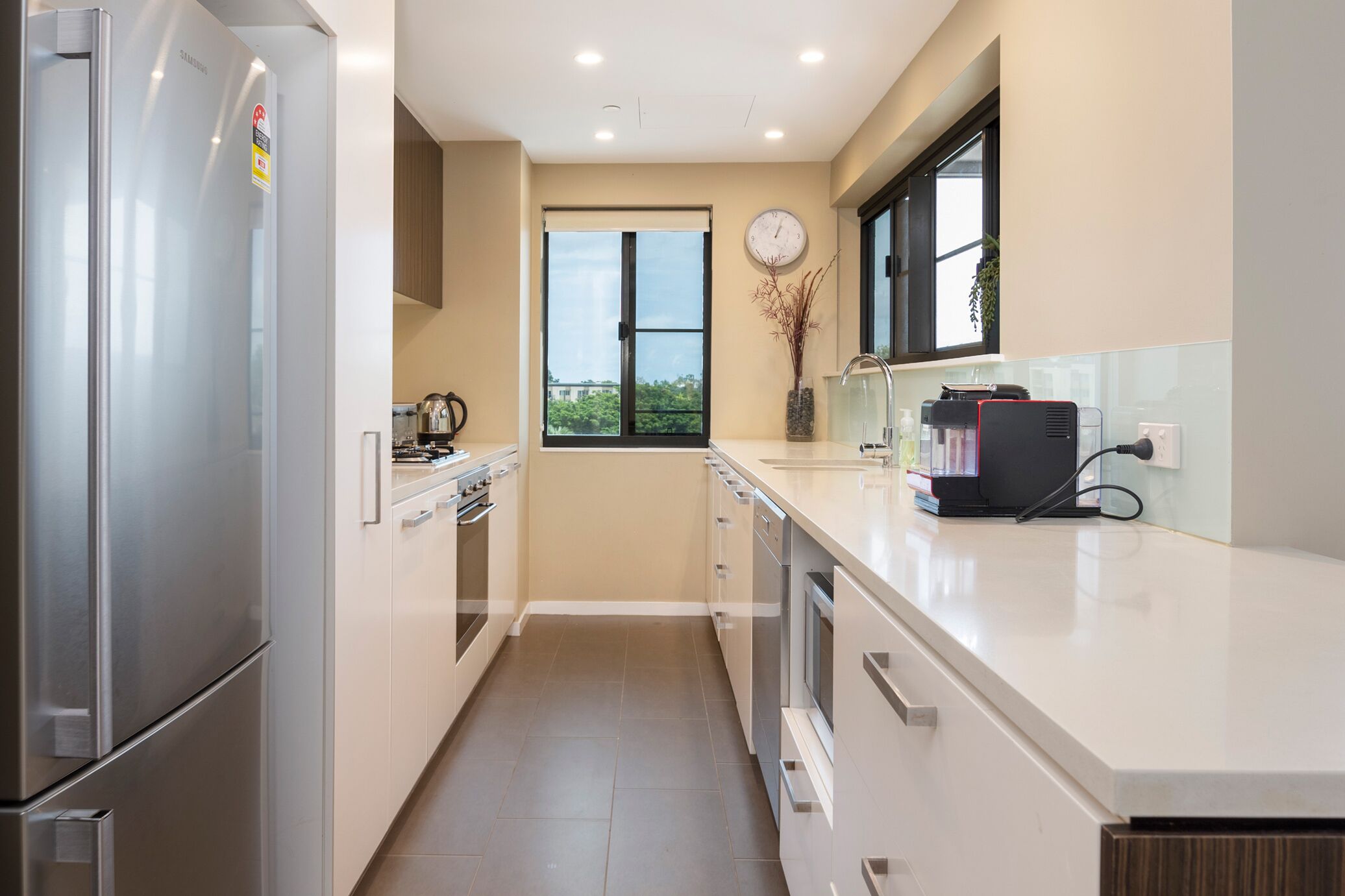 A modern kitchen with stainless steel appliances, a window with a view, and a clock on the wall.