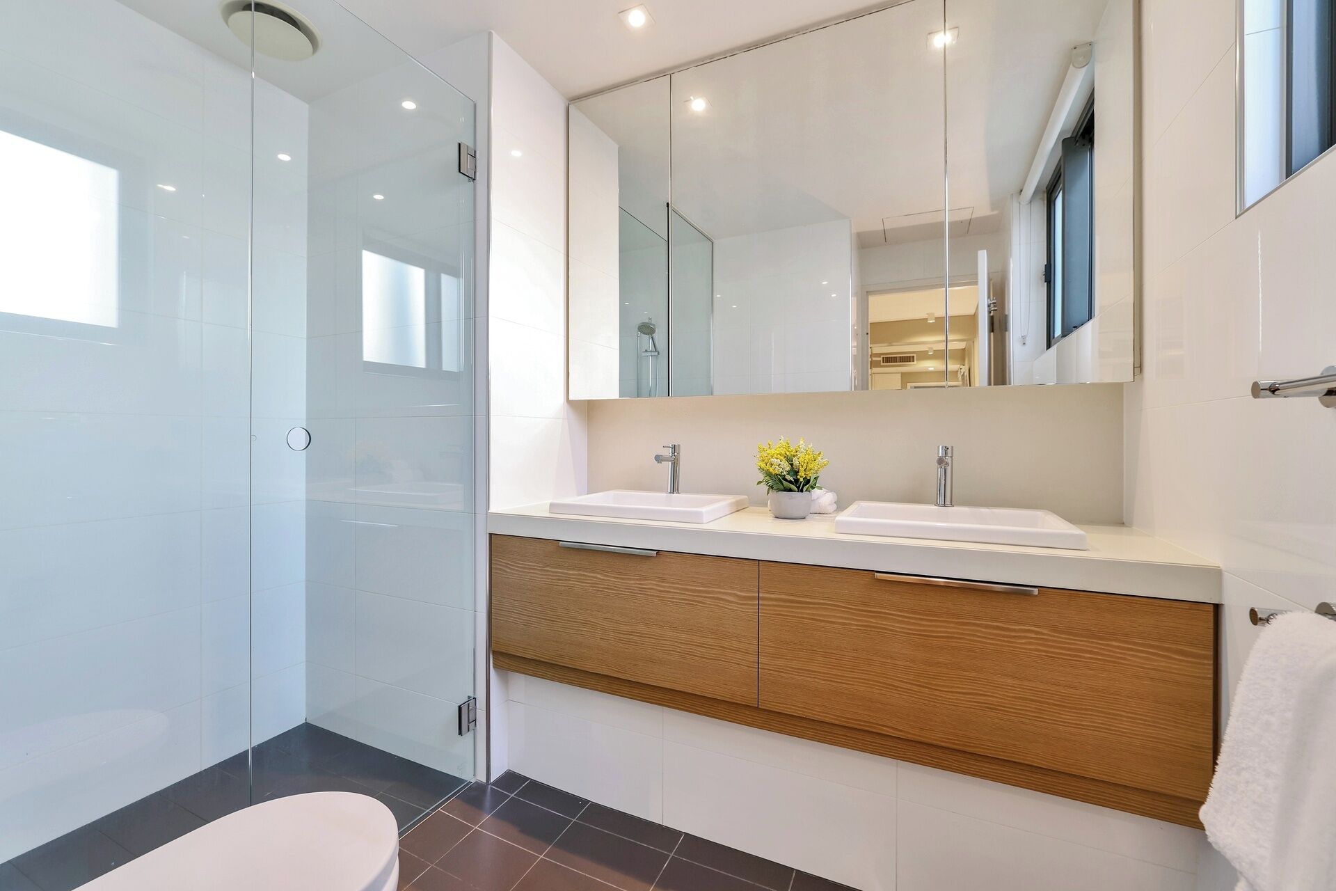 Un baño moderno con cabina de ducha de vidrio, tocador de madera con dos lavamanos y un espejo grande sobre el tocador.